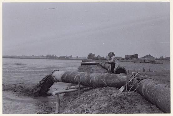 Het land van boer Jaap Kool wordt opgespoten in juni 1959. Op de achtergrond is de boerderij te zien en rechts de Broekkade. Met mogelijke verschuivingen van de ondergrond ook buiten het op te spuiten terrein, is rekening gehouden. Daarom werden de perskaden op circa 100 meter van de rijksweg A20 en op circa 70 meter van de boezemkade langs de Vlaardingse Vaart aangelegd. Fotograaf: A.J. van Druten, Collectie Stadsarchief Vlaardingen, T653-034.